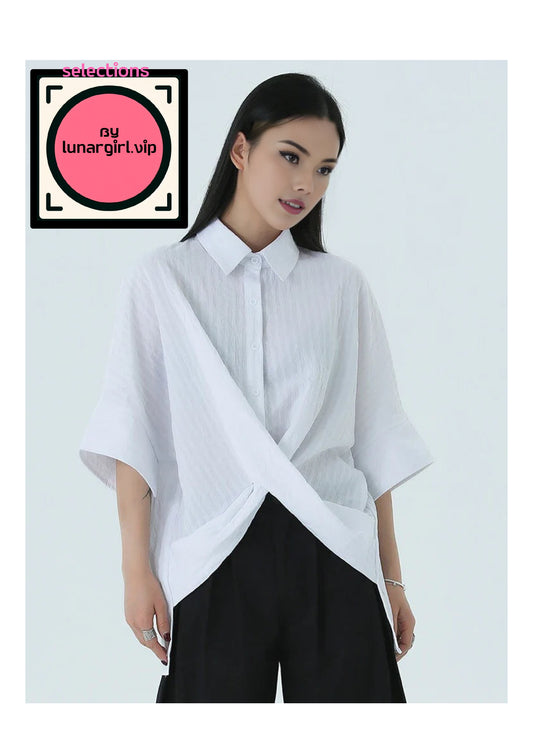 This white shirt features a crisp, pointed collar that adds a touch of formality, making it suitable for both casual and semi-formal occasions for warm weather or layering.
One of the most distinctive features of this shirt is its asymmetrical cut. The front showcases an innovative design where one side drapes across the body and is secured at the waist, creating a unique diagonal line that draws attention to the midsection. This asymmetry not only adds visual interest but also enhances the shirt’s modern a